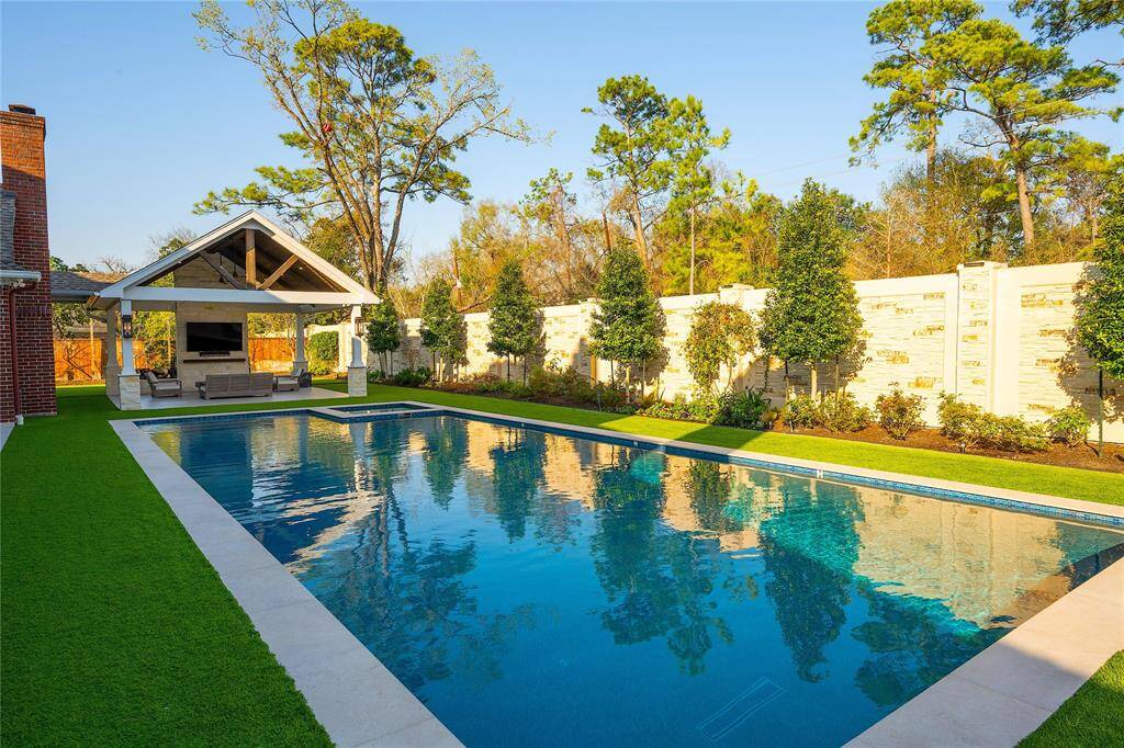 Lush, professionally landscaped greenery, including mature trees and meticulously arranged plants, creates a serene and private ambiance, enhancing the backyard’s resort-like atmosphere.