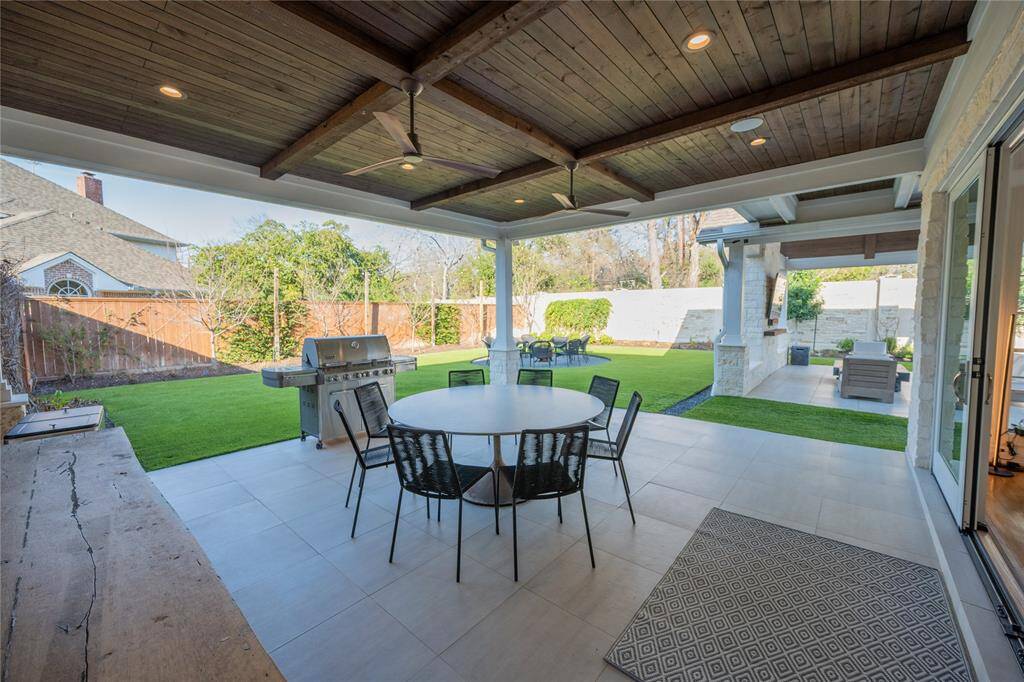 This beautifully designed outdoor living space features a covered patio with a rich, dark-stained wood plank ceiling, recessed lighting, and a sleek ceiling.