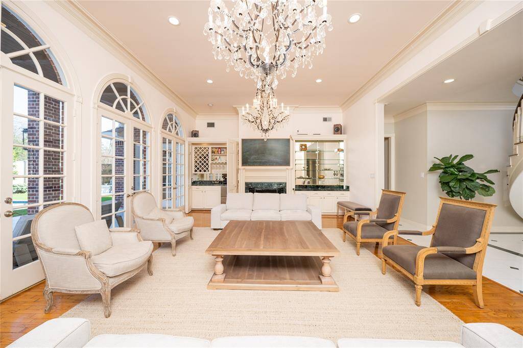 This elegant formal living room exudes timeless sophistication, featuring stunning crystal chandeliers, expansive arched windows that flood the space with natural light, intricate millwork, and a cozy fireplace.