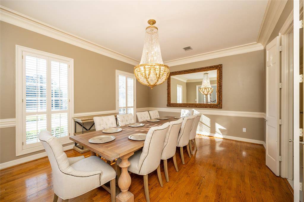 This elegant formal dining room exudes sophistication, featuring a stunning chandelier that casts a warm, inviting glow, complemented by abundant natural light, rich hardwood floors,