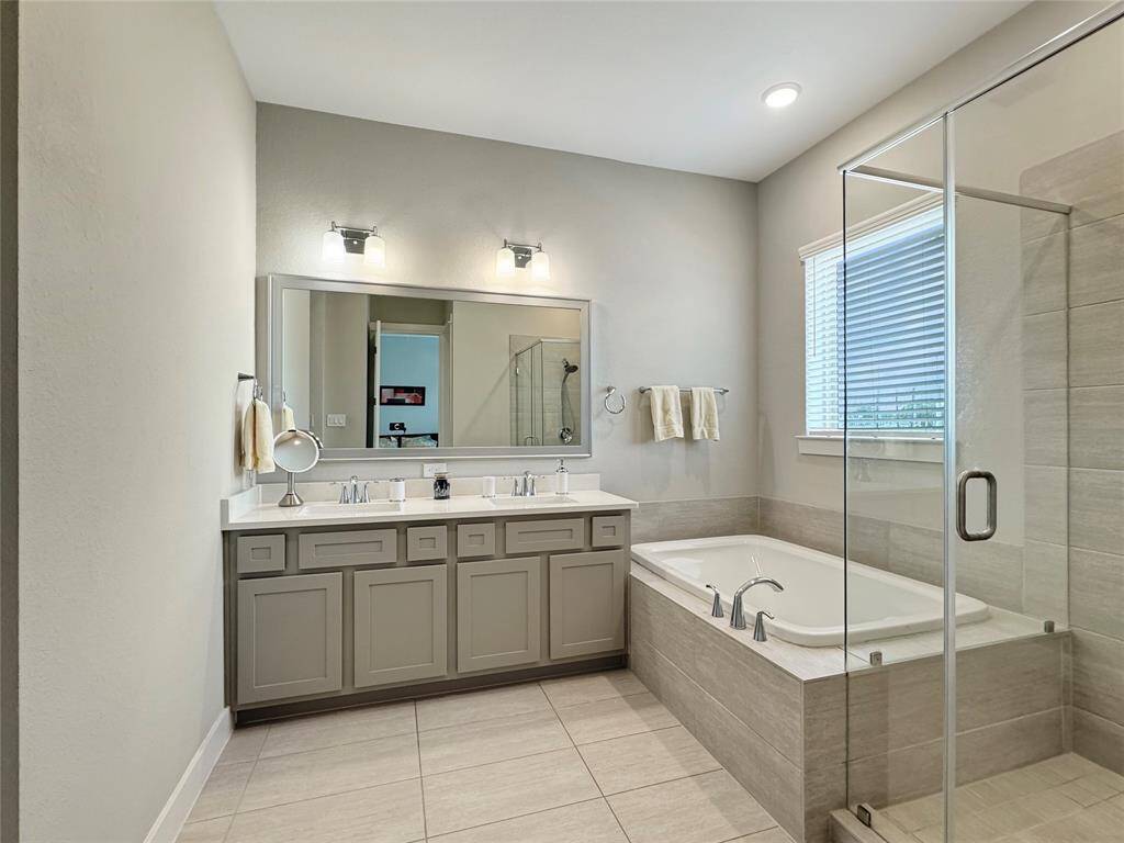 Spacious primary bathroom features a double vanity with ample storage, a large mirror, a luxurious soaking tub, and a modern glass-enclosed shower. The neutral tones and recessed lighting create a bright and inviting atmosphere.