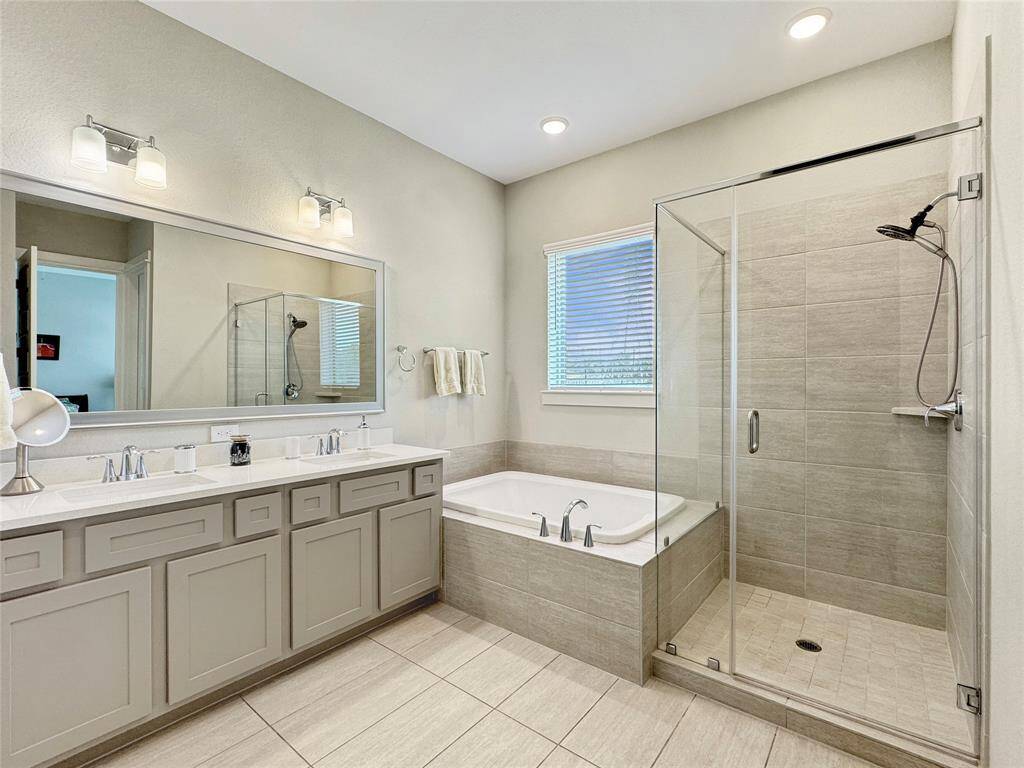 Spacious primary bathroom features a double vanity with ample storage, a large mirror, a luxurious soaking tub, and a modern glass-enclosed shower. The neutral tones and recessed lighting create a bright and inviting atmosphere.