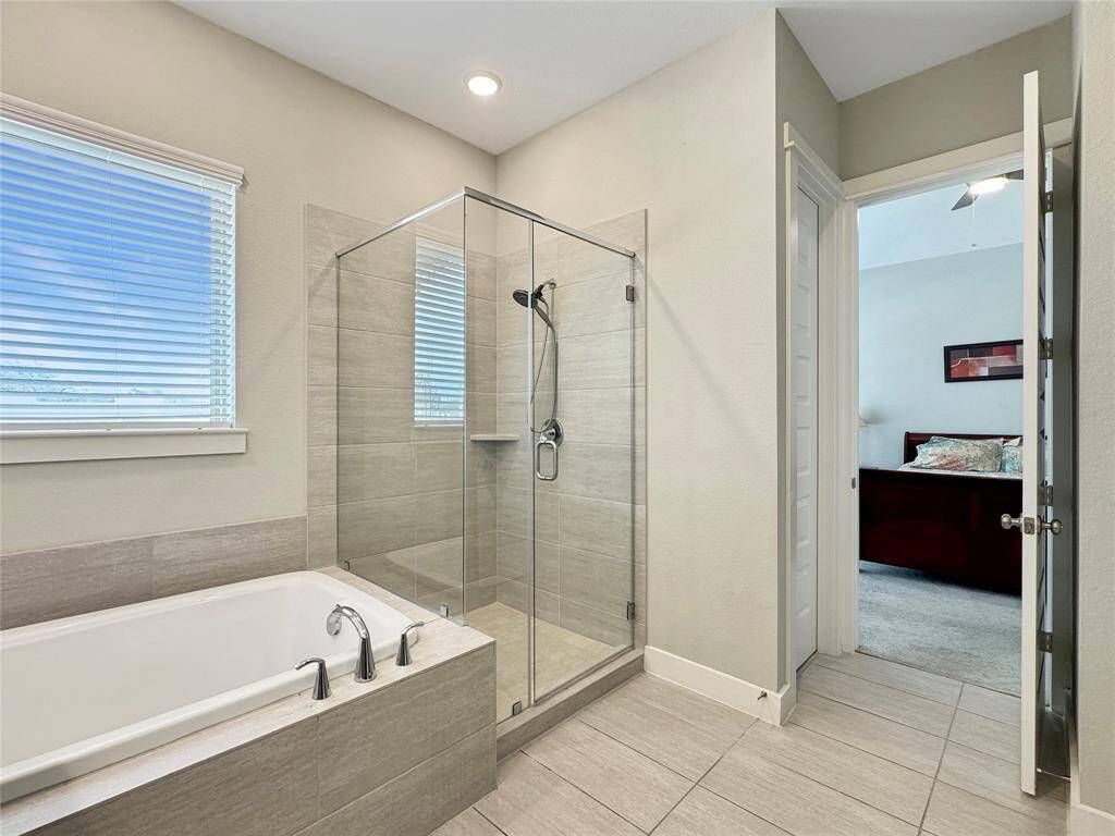 Spacious primary bathroom features a double vanity with ample storage, a large mirror, a luxurious soaking tub, and a modern glass-enclosed shower. The neutral tones and recessed lighting create a bright and inviting atmosphere.