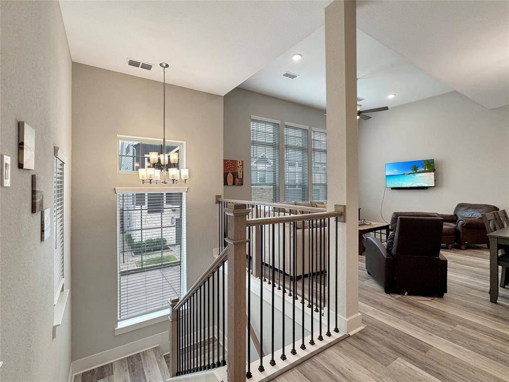 Enjoy a modern, open-concept living area with high ceilings and abundant natural light. A stylish staircase with sleek railings leads to the upper floor. The space features contemporary flooring, a cozy seating area, and a wall-mounted TV for entertainment. (TV not included)