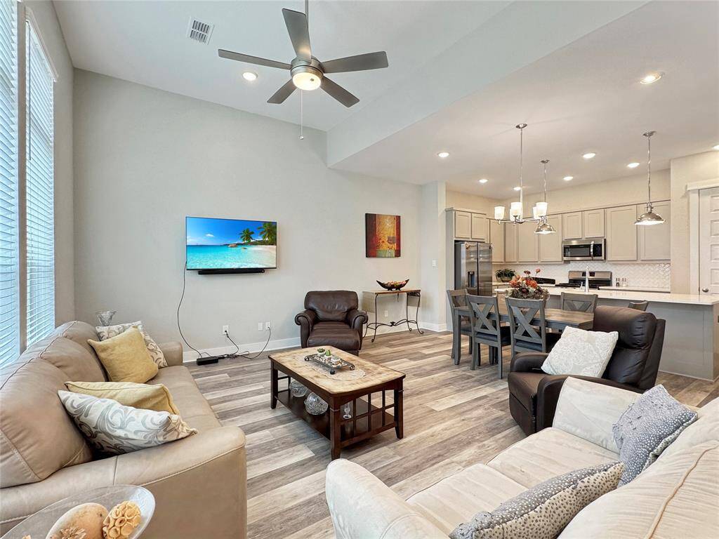 This open-concept living area features a spacious layout with a cozy seating arrangement, modern kitchen, and stylish dining space. It has ample natural light, sleek flooring, and contemporary fixtures, creating an inviting and functional atmosphere for family living and entertaining.