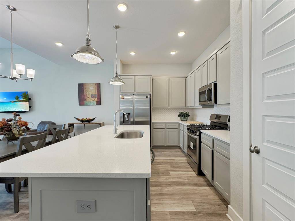 This modern kitchen features sleek cabinetry, stainless steel appliances, and a spacious island with a sink. The open layout flows into a dining area with stylish lighting and contemporary decor.