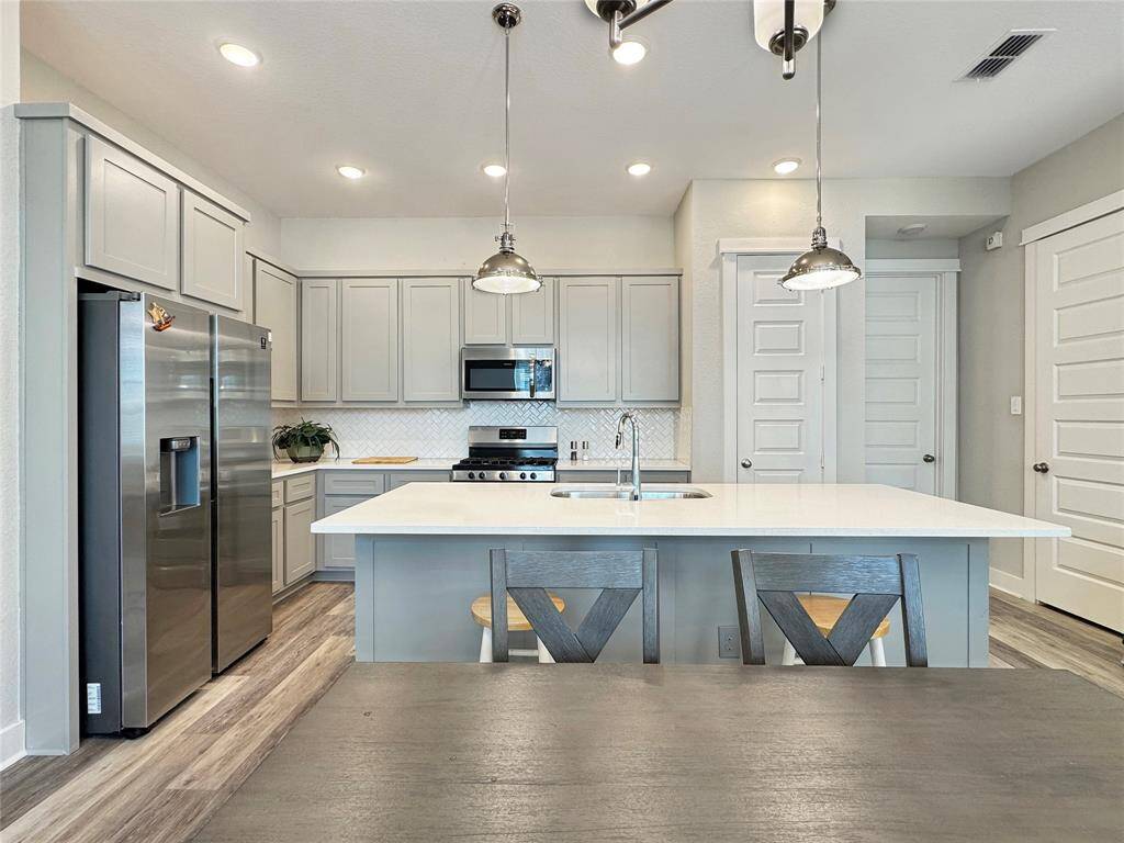 This modern kitchen features sleek gray cabinetry, stainless steel appliances, and a spacious island with pendant lighting. The open layout and bright lighting create an inviting atmosphere perfect for cooking and entertaining.