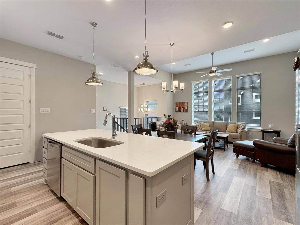 Modern, open-concept kitchen and living area. The kitchen features a large island with a sink, pendant lighting, and ample cabinetry. The living area is bright with large windows, stylish flooring, and comfortable seating. Perfect for entertaining and family living.