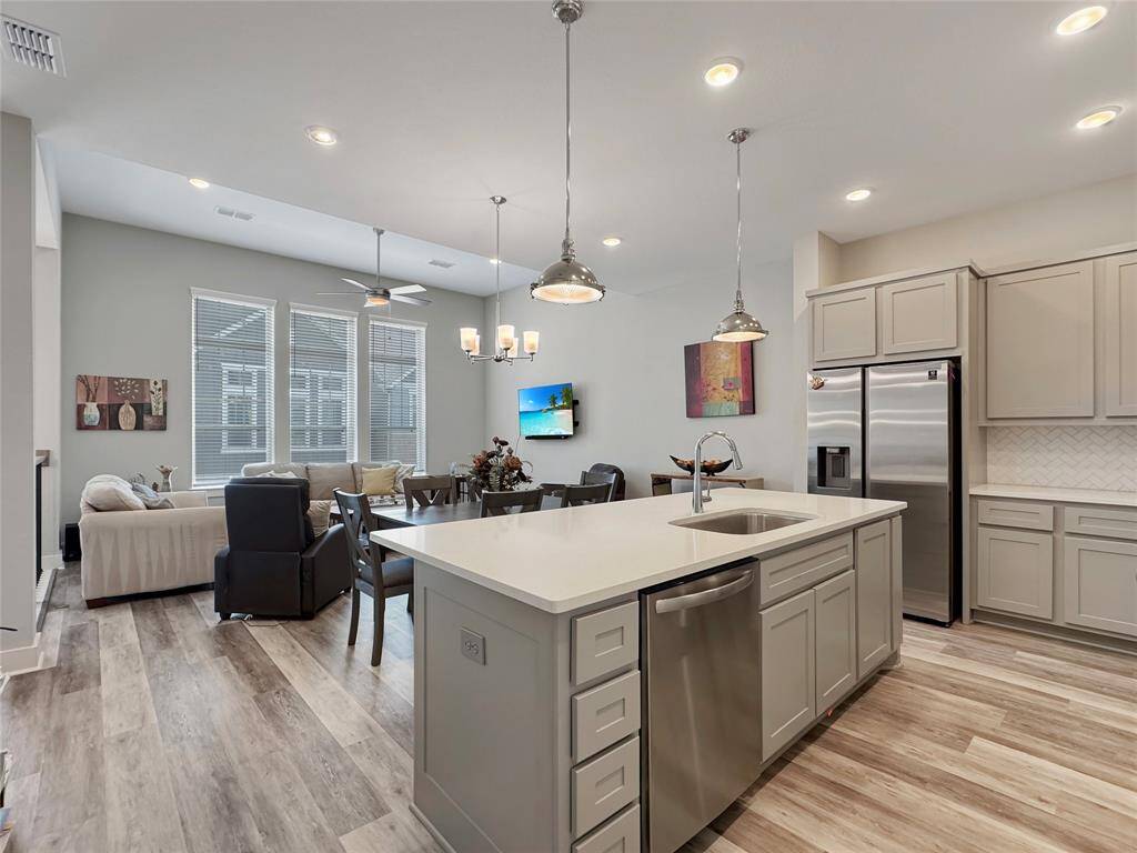 Modern, open-concept kitchen and living area with light wood flooring. The kitchen features a large island with a sink, stainless steel appliances, and sleek cabinetry. The living area is bright with large windows, and there's a cozy seating arrangement, making it ideal for entertaining.