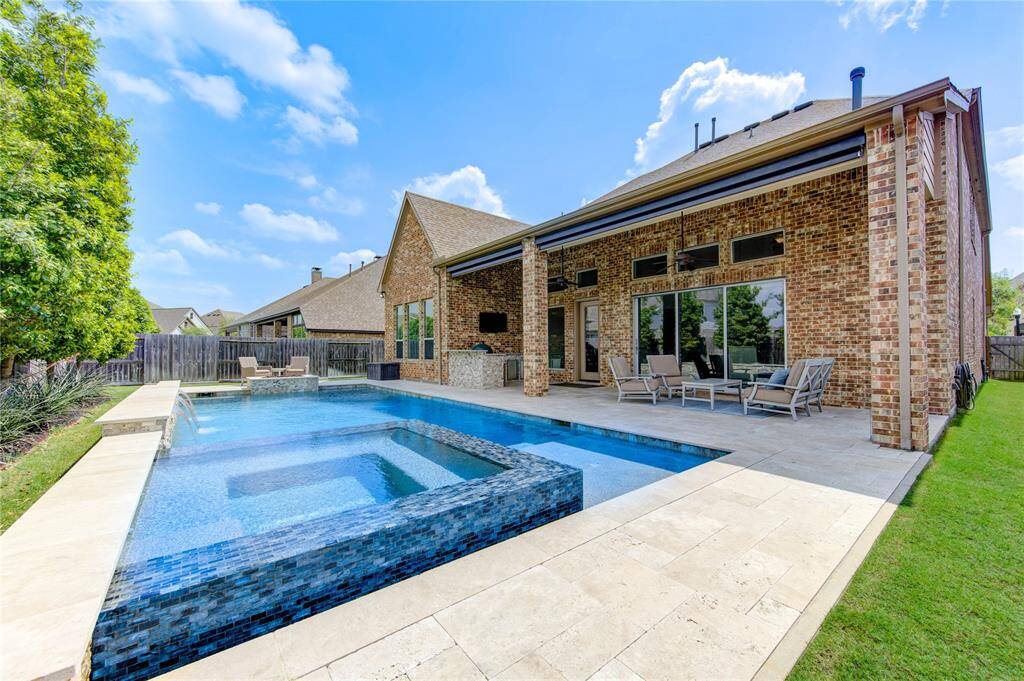 The luxurious swimming pool, hot tub, and spacious patio area provides a stylish scene for this brick exterior home. All of this is complemented by ample seating for outdoor relaxation and entertainment.