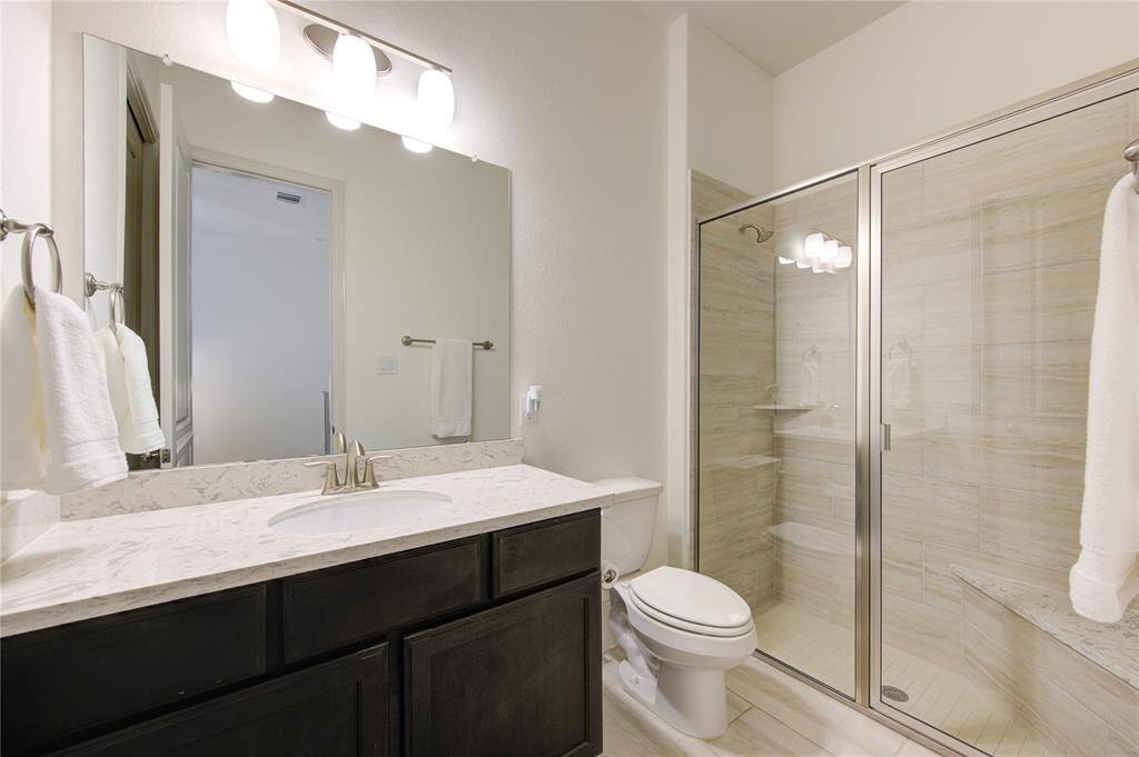This bathroom #2 features a spacious glass-enclosed shower, a sleek marble countertop with a modern sink, and ample lighting.