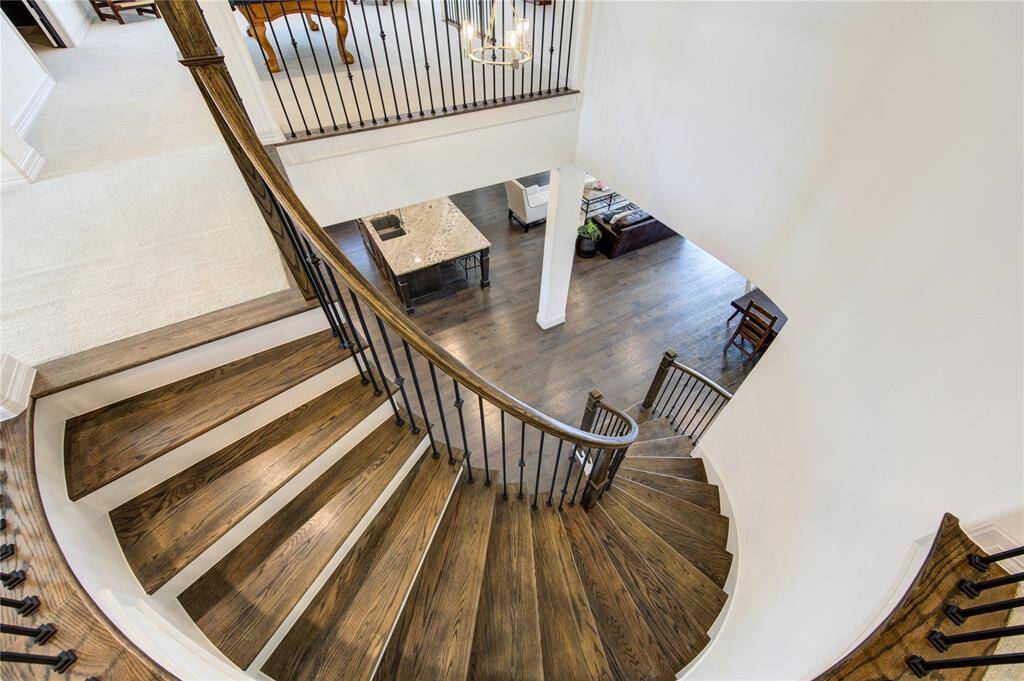 Elegant curved staircase with dark wood steps and sleek black railings, descending to an open living area with hardwood floors and a view of the modern kitchen.