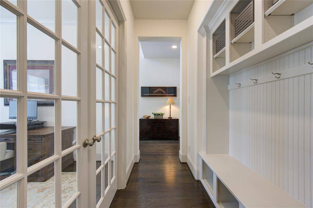 Bright and inviting hallway with glass-paneled doors leading to a cozy study and a mudroom featuring built-in storage with hooks and shelves.
