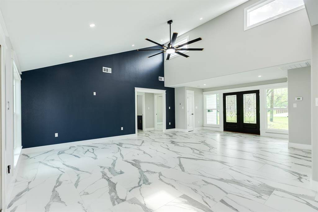 Living room has expansive ceilings, tons of natural light, and gorgeous statement ceiling fan. Hallway leads to guest bath and secondary bedrooms.