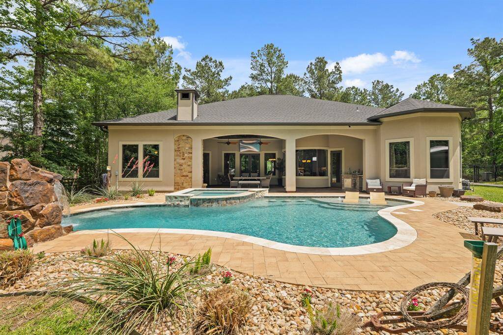 This photo showcases a modern home with a spacious backyard featuring a luxurious pool and spa, surrounded by a landscaped patio and lush trees, offering a blend of relaxation and privacy.