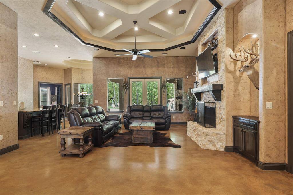 Spacious family room featuring a cozy fireplace, elegant coffered ceiling, and abundant natural light from large windows. Perfect for relaxation and entertaining.