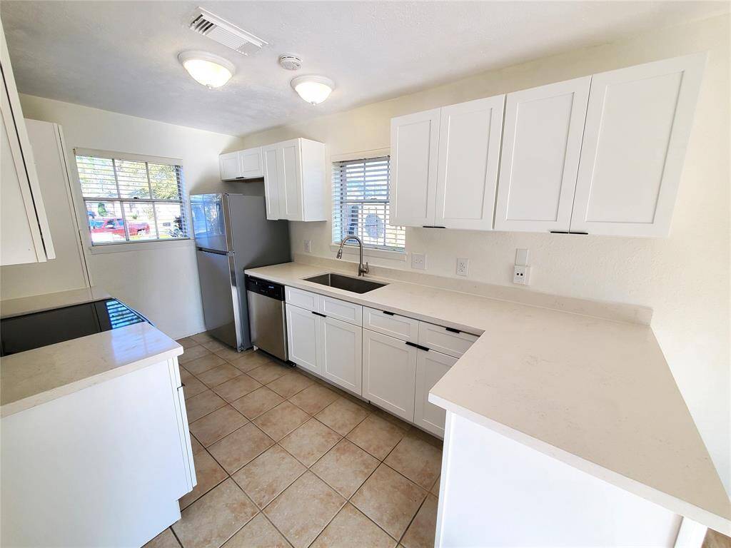 This kitchen features a clean, bright design with white cabinets and countertops. It includes modern appliances, a double window for natural light, and tiled flooring. The layout is efficient and offers ample storage and counter space.