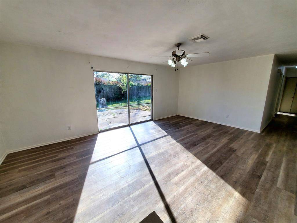 Spacious living area with wood flooring, ample natural light from large sliding doors leading to a backyard, and a ceiling fan for comfort. Neutral walls offer a blank canvas for personalization.