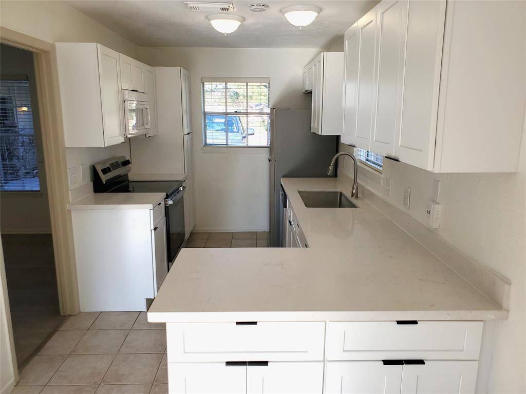 This kitchen features sleek white cabinetry, modern appliances, and a spacious countertop. It has a bright and clean look with natural light from the window, creating an inviting space for cooking and entertaining.