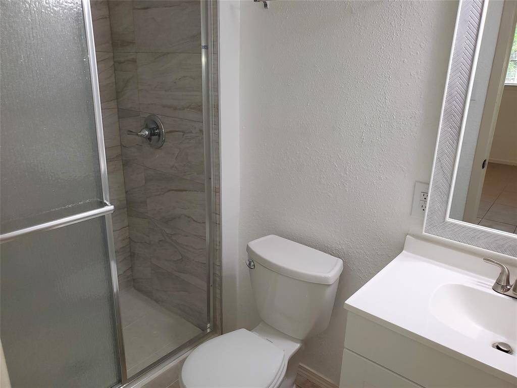 This photo shows a modern bathroom with a glass-enclosed shower featuring tiled walls, a toilet, and a sink with a sleek faucet and mirror. The space is bright and minimalistic.