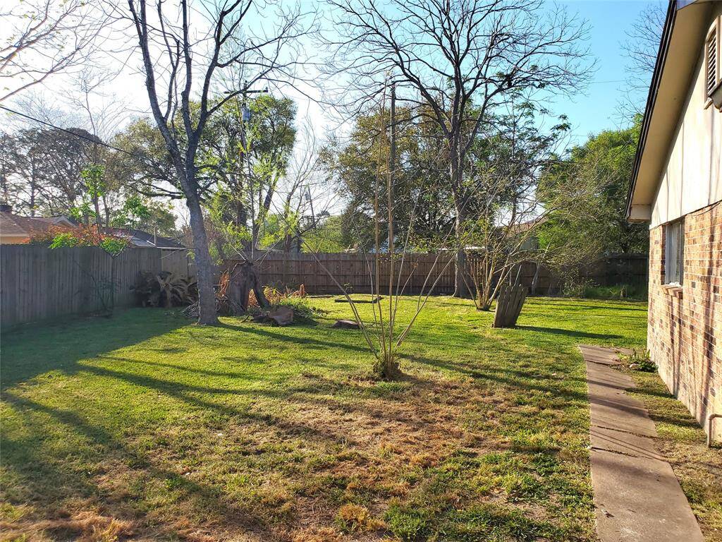Spacious backyard with mature trees and a wooden fence, providing a private, shaded area ideal for outdoor activities and gardening.