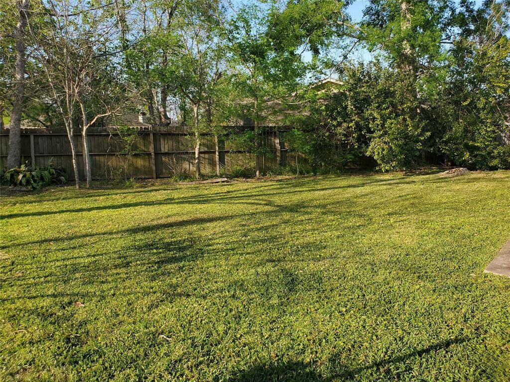 Spacious backyard with lush green grass and mature trees along a wooden fence, offering privacy and a serene outdoor space.