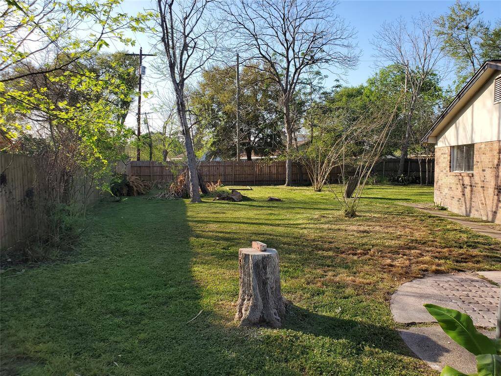 Spacious backyard with mature trees and a wooden fence for privacy. The area features a mix of grass and paved pathways, ideal for outdoor activities and gardening.