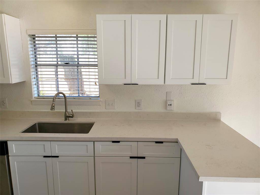 This kitchen features modern white cabinetry, a sleek stainless steel sink, and a polished countertop. A window above the sink allows for natural light, enhancing the clean, bright aesthetic.