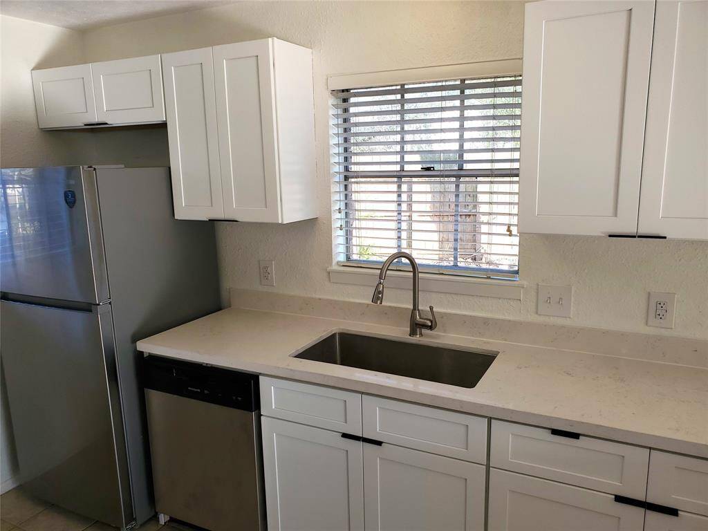 This kitchen features modern white cabinetry, a sleek stainless steel sink, and matching appliances, including a refrigerator and dishwasher. The window above the sink provides natural light and a view outside.