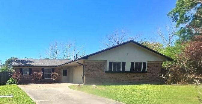 This is a single-story brick home with a gable roof, featuring a two-car garage. It has a spacious driveway and is surrounded by a well-maintained lawn with some trees and shrubs.