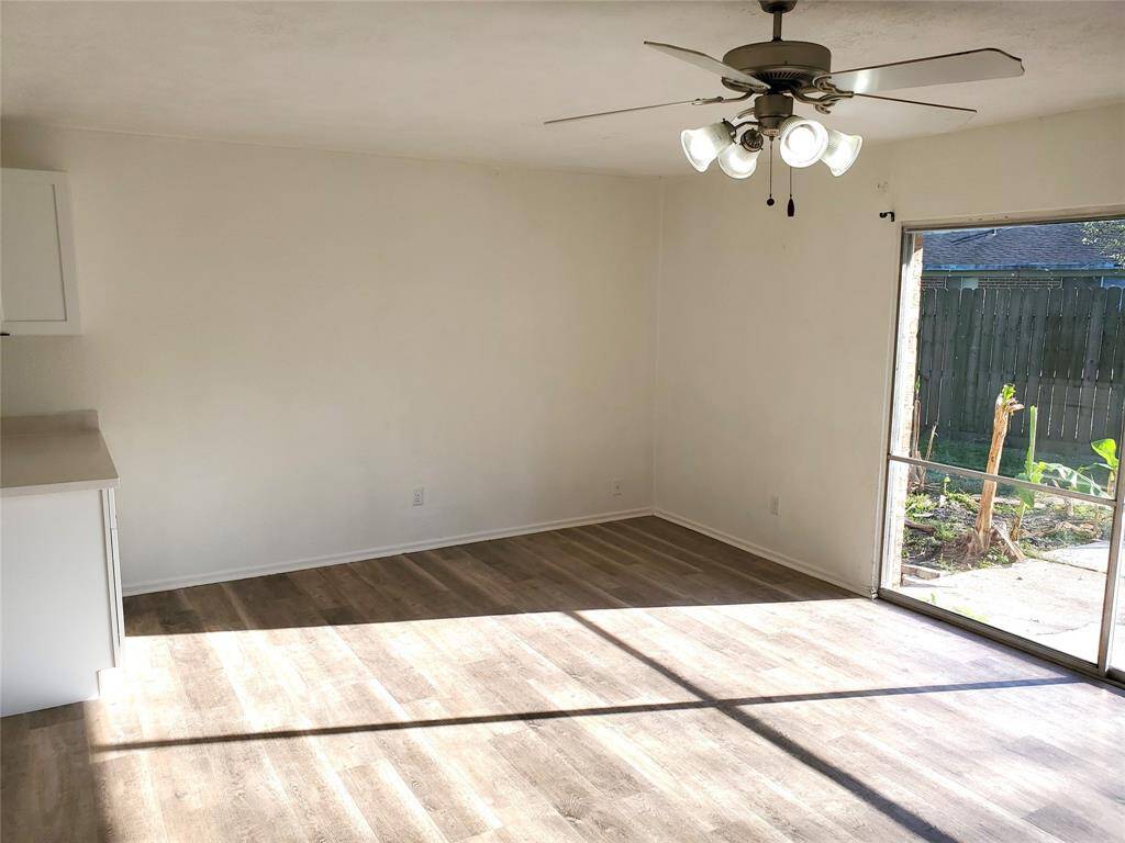Bright room with light wood flooring and a ceiling fan. Large window provides natural light and a view of the backyard. Simple and inviting space.