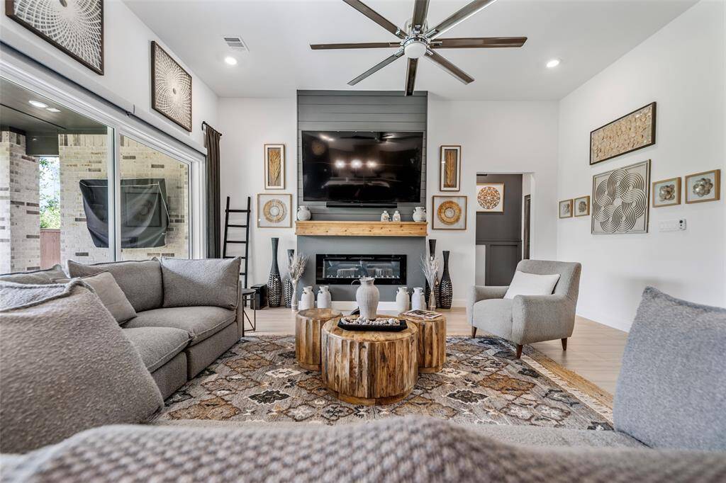 The spacious great room is the heart of the home, featuring a sleek steel ceiling fan, a modern electric fireplace for cozy ambiance, and a seamless open layout that flows effortlessly into the kitchen—perfect for both everyday living and entertaining.