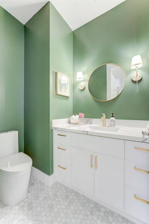 This gorgeous green half bathroom has custom pendant lighting, gold  hardware, white cabinetry, quartz  countertops, and chic patterned tile flooring.