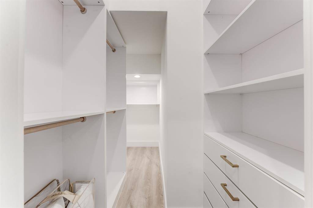 The walk-in closet features built-in shelving and drawers with gold accented hardware.