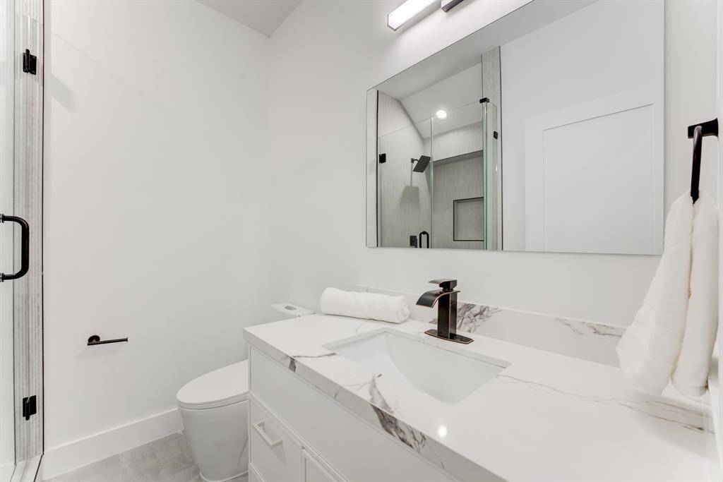 Ensuite bathroom features quartz countertops, black accented hardware and large frameless mirror.