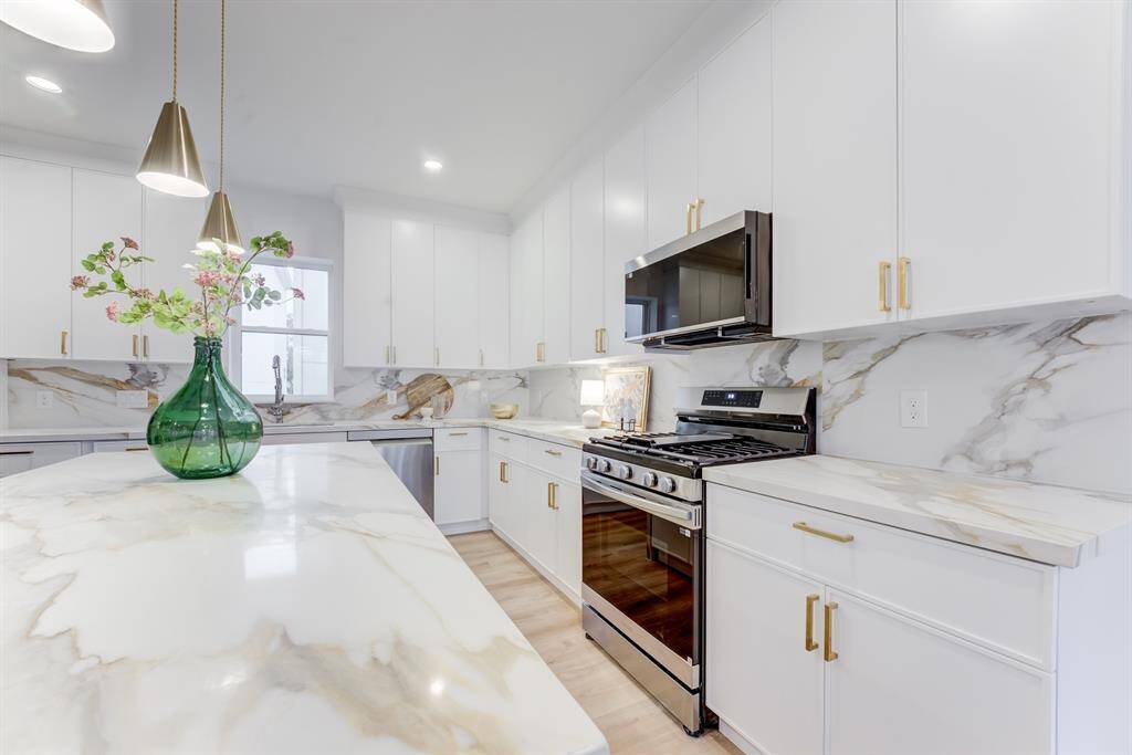 This stunning kitchen features gold  hardware, quartz countertops, gas  range, and stainless steel  appliances. There is plenty of  storage space in the cabinets