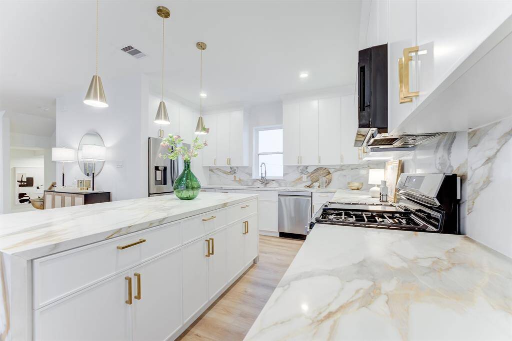 This stunning kitchen features gold  hardware, quartz countertops, gas  range, and stainless steel  appliances. There is plenty of  storage space in the cabinets.