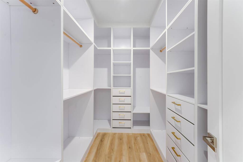 This large custom built closet  features built-in drawers with gold  accented hardware, storage space,  and clothes hanging rods.