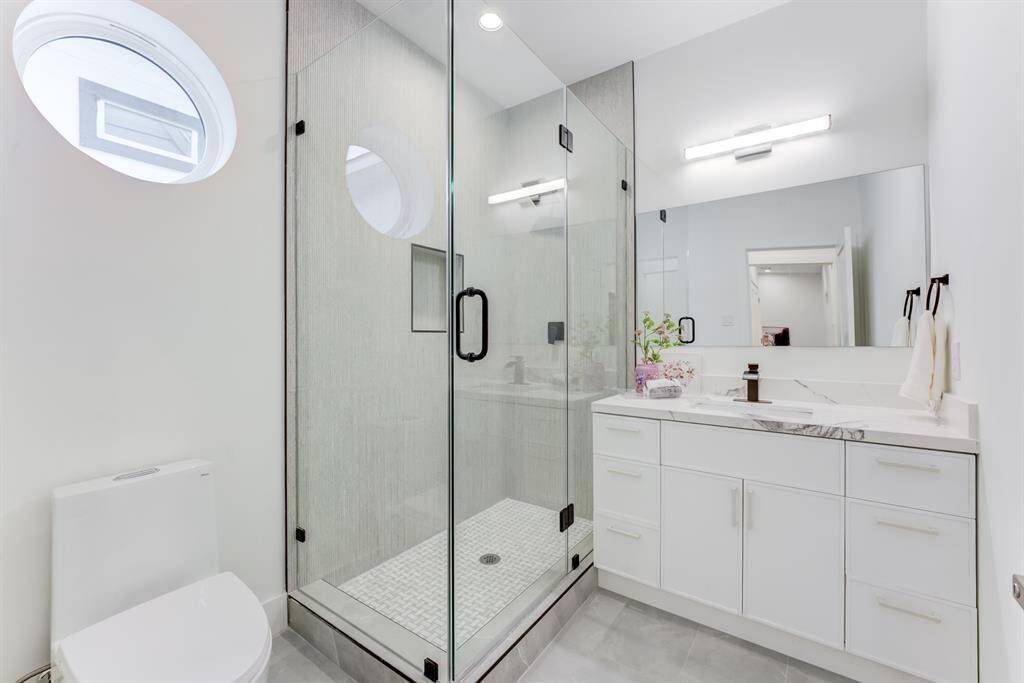 The secondary en-suite bathroom has a frameless neutral toned shower, large mirror, quartz countertops, and elegant white cabinetry for a timeless bathroom feel.