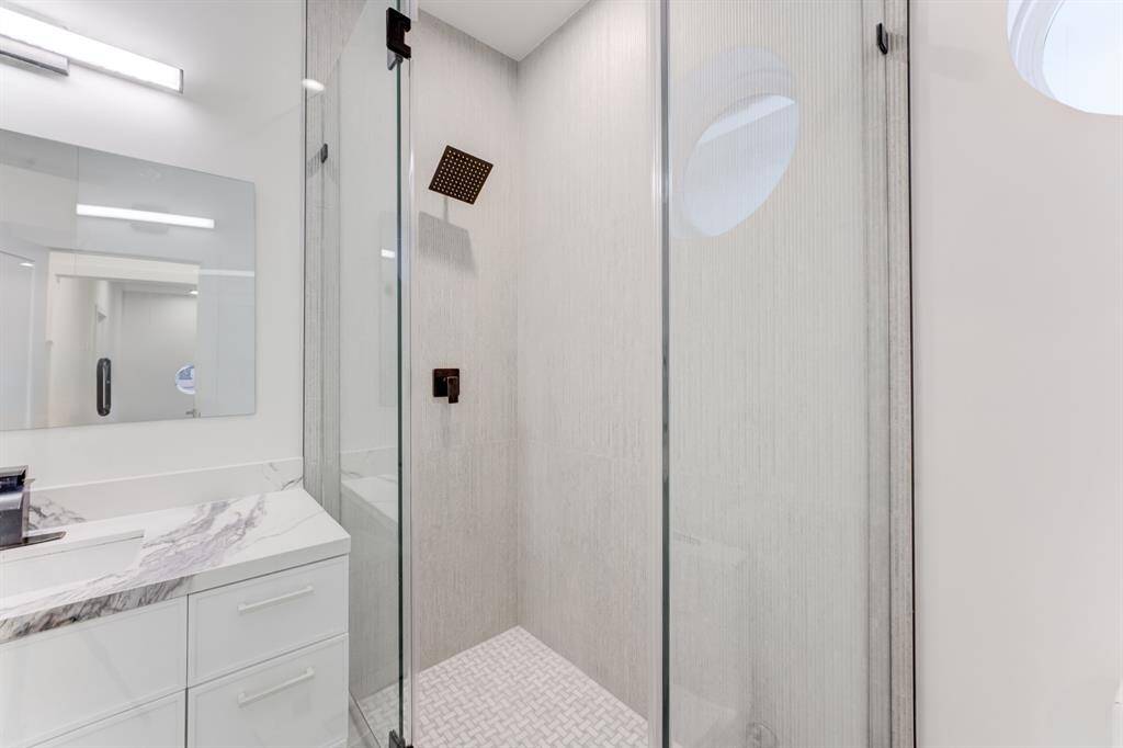 Frameless glass shower door with black hardware and neutral toned tile.