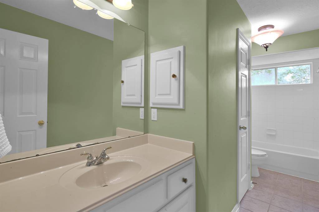 This secondary bathroom has an extended counter and cabinet area with white wood inset medicine cabinet. It has a tub/shower combo overlooking back yard and a storage/linen closet.