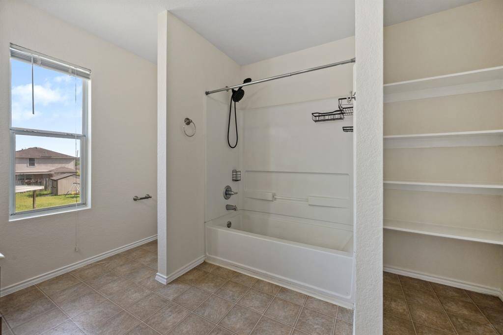 En-suite primary bath with a large vanity and tub/shower combo and built-in shelves.