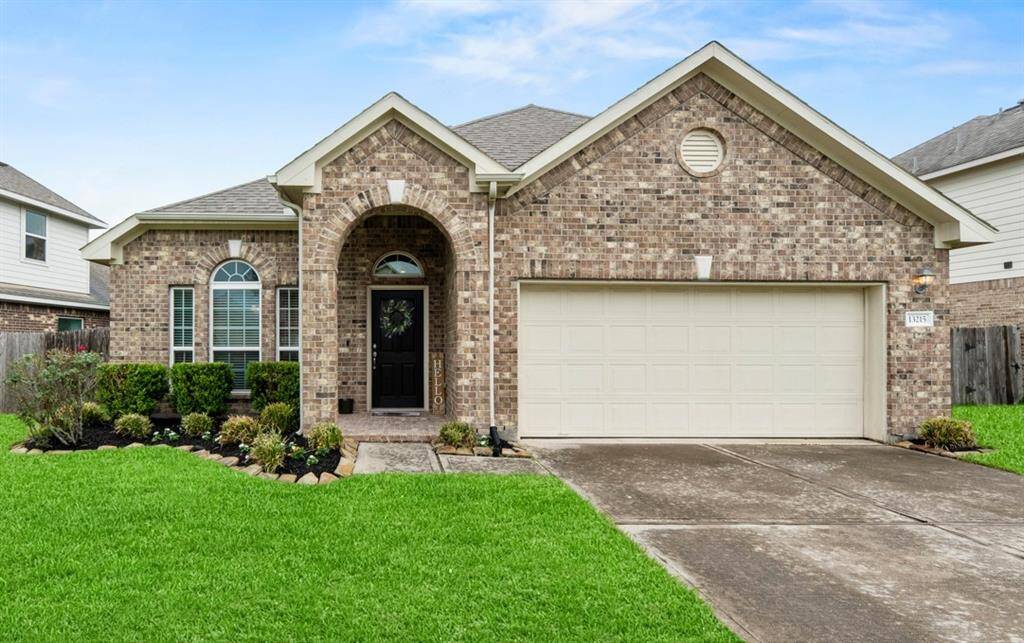 This charming brick home features a well-maintained lawn and a welcoming arched entryway.