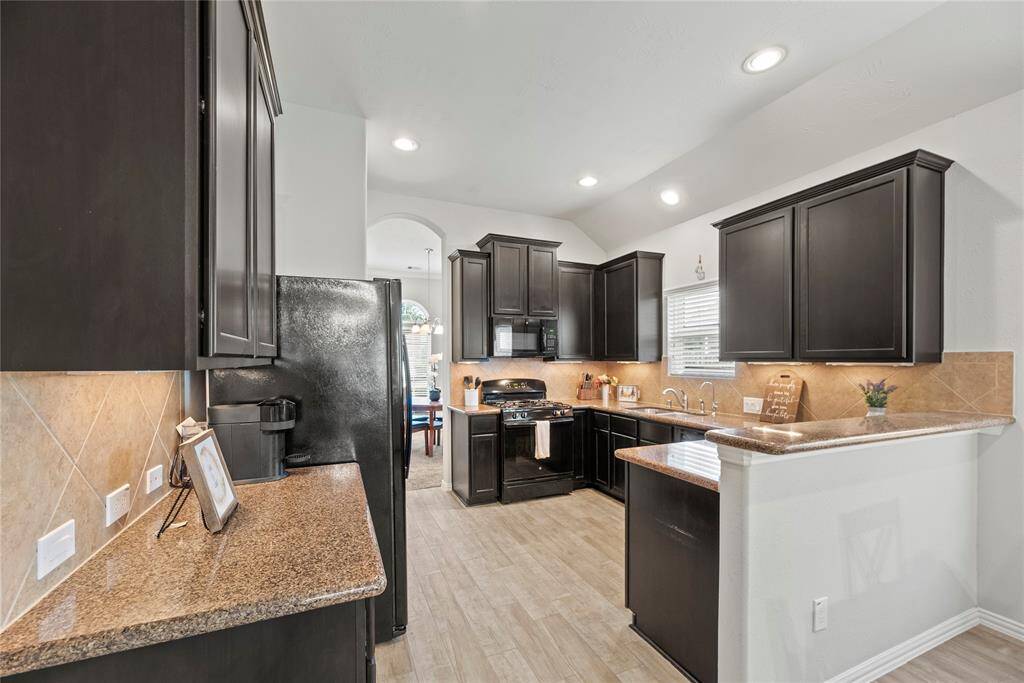 This modern kitchen features sleek dark cabinetry, granite countertops. It has a tile backsplash, recessed lighting, and a small breakfast bar, creating a stylish and functional space.