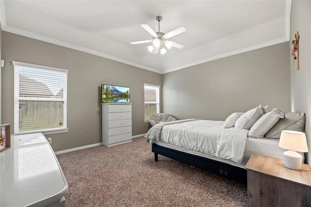 This bedroom features ample natural light from two windows and ceiling fan. The room is spacious and well-lit, offering a cozy and inviting atmosphere.
