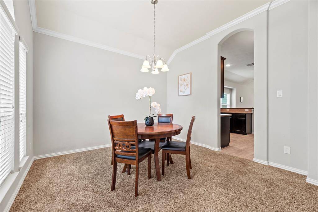 This formal dining area has a high ceiling and neutral walls. The large windows provide ample natural light, and an archway leads to the kitchen, enhancing the open feel.