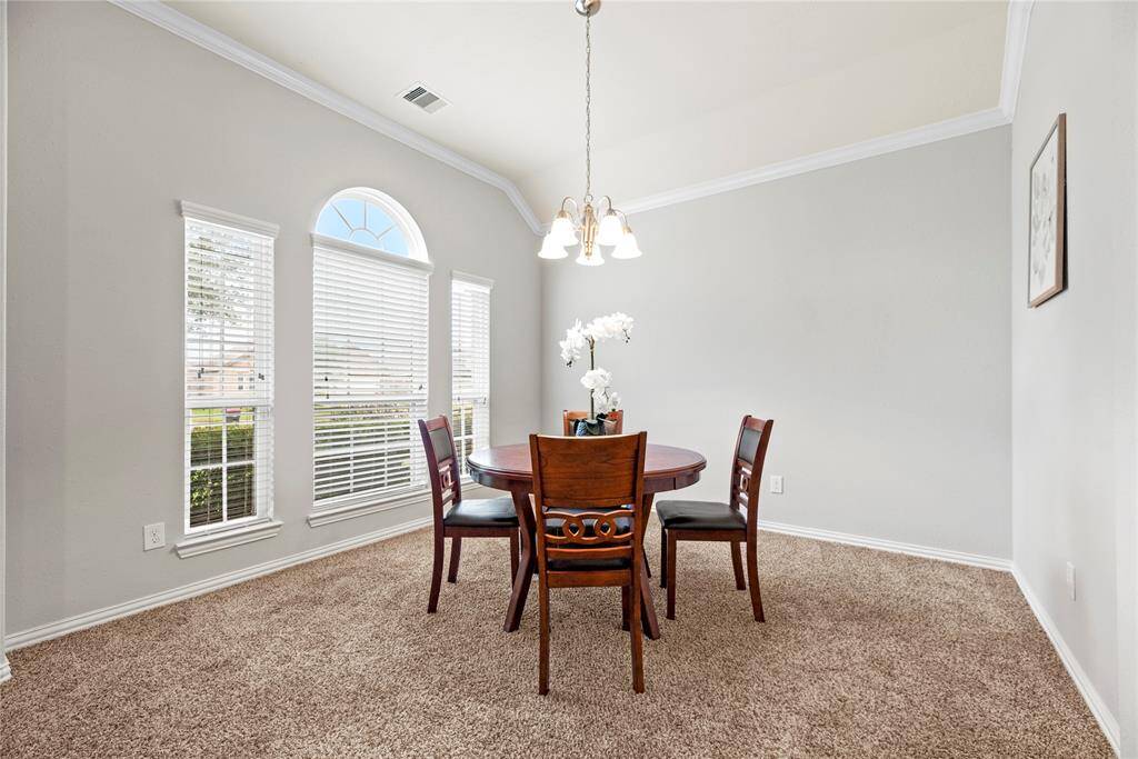 Bright dining area with large windows and soft carpeting. Features a round table with four chairs, neutral wall colors, and a central light fixture.