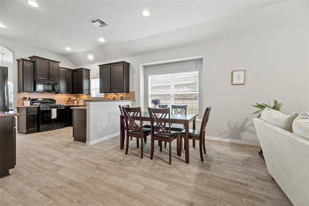 Open-concept kitchen and dining area with sleek dark cabinets, and a cozy dining nook by a large window.