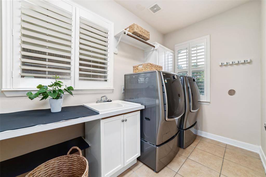 Spacious utility room is both practical and polished, featuring ample counter space, upper cabinetry, a built in sink, and plenty of room for laundry and storage needs.