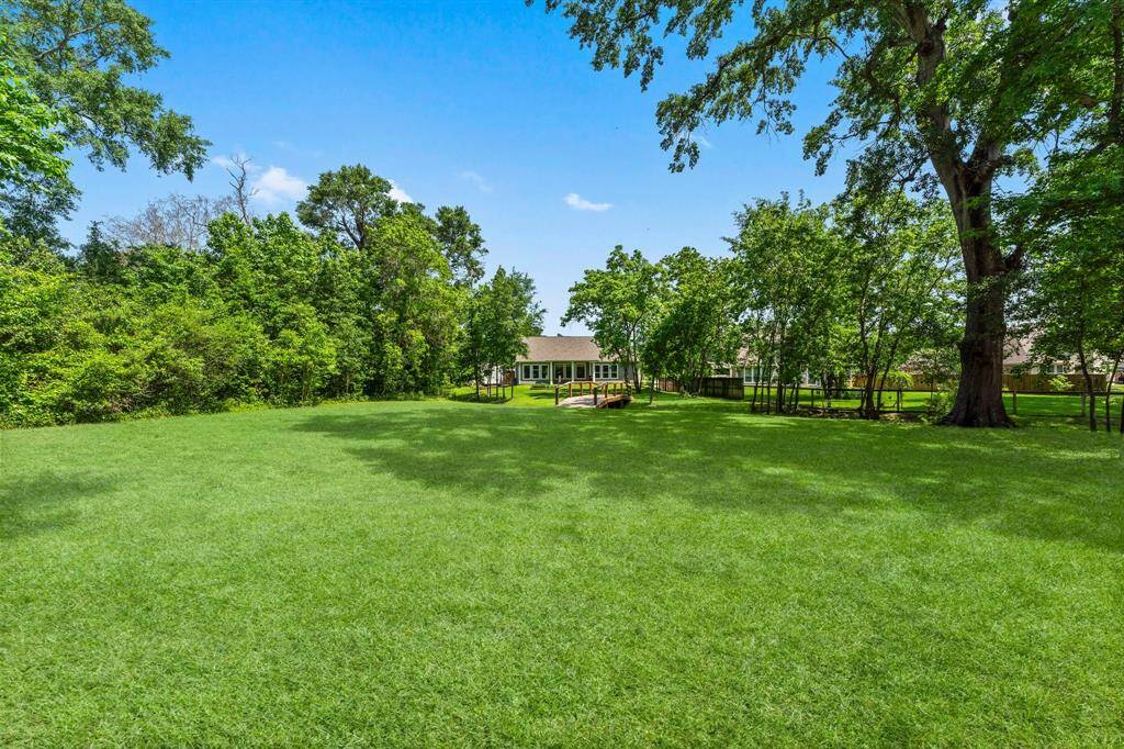 Sprawling 1-acre lot surrounded by mature trees. View from the back of the property looking on to the bridge and back of the home.